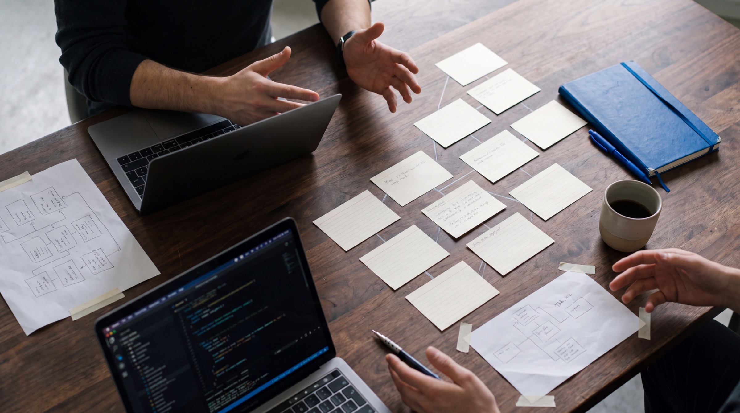 A team at a walnut table with index cards laid out as a tree beside two laptops and a blue notebook